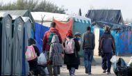 Migrants carry their belongings as they walk in an alley near tents and makeshift shelters on the eve of the evacuation and dismantlement of the camp called the 