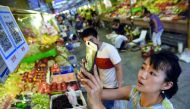  A woman making purchases by scanning QR codes using her smartphone at a fruit stall in a market in Beijing