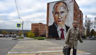 An elderly woman crosses a road in front a mural painting depicting Russian President Vladimir Putin, on the wall of a house, in the town of Kashira, some 115 km southeast of Moscow, on October 16, 2017.  AFP / Vasily Maximov