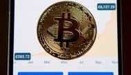 A gold plated souvenir Bitcoin coin is arranged for a photograph on a smart phone displaying current value of a single bitcoin, and options to buy or sell, on an app for the digital asset broker, Coinbase, in London on November 20, 2017.   AFP / Justin TA