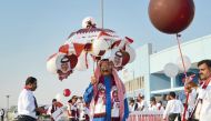 A man holding an umbrella with the pictures of Emir H H Sheikh Tamim bin Hamad Al Thani at Asian Town as part of National Day celebrations. 