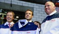 French President Emmanuel Macron (centre) holds a Toyota staff uniform marked with his name as he poses with Toyota Motor Manufacturing France (TMMF) Director Luciano Biondo (right) and Didier Leroy, Executive Vice President of Toyota Motor Corporation, d