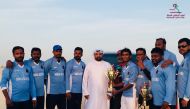 Doha Riders winners of the National Sport Day four-team cricket tournament pose for a picture with an official.