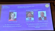 A screen displays portraits of Frances H Arnold of the United States, George P Smith of the United States and Gregory P Winter of Great Britain during the announcement of the winners of the 2018 Nobel Prize in Chemestry at the Royal Swedish Academy of Sci