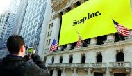 A man takes a photo of the New York Stock Exchange (NYSE) with a Snap Inc logo hung on the front of it.