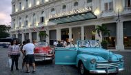 Tourists stand next to an old American car in front of the Gran Manzana Hotel in Havana, on February 11, 2019.  AFP / Yamil Lage 