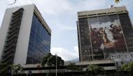 The logo of the Venezuelan state oil company PDVSA is seen next to a mural depicting late President Hugo Chavez at a gas station in Caracas, March 2, 2017. Reuters/Carlos Garcia Rawlins