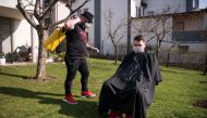 Kosovo hairdresser Driton Kameri (L) wears a facemask as he disinfects a client ahead of a haircut in his garden on March 30, 2020 in Pristina during the time of the COVID-19 pandemic. AFP / Armend NIMANI