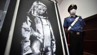 A policeman stands guard near a piece of art attributed to Banksy, that was stolen at the Bataclan in Paris in 2019, and found in Italy, ahead of a press conference in L'Aquila on June 11, 2020.  AFP / Filippo MONTEFORTE 