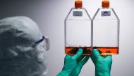 A lab technician wearing Personal Protective Equipment (PPE) looks at reagent bottles before performing vaccine tests at a French pharmaceutical company Sanofi's laboratory in Val de Reuil on July 10, 2020. / AFP / JOEL SAGET
