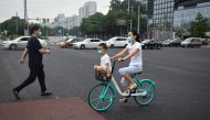 A woman and child wearing face masks commute on a public share bicycle on a street in Beijing on August 20, 2020. (AFP / WANG ZHAO)