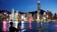 FILE PHOTO: A man wearing a protective face mask takes a photo of the sunset at Tsim Sha Tsui waterfront as skyline buildings stand across Victoria Harbor following the coronavirus disease (COVID-19) outbreak in Hong Kong, China July 28, 2020. REUTERS/Tyr