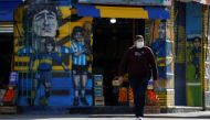 A man wearing a face mask as a preventive measure against the coronavirus disease (COVID-19) walks past a grocery store painted with graffitis depicting Diego Maradona, Carlos Tevez and Juan Roman Riquelme in Buenos Aires, Argentina May 31, 2021. REUTERS/