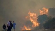 People stand on the road during a wildfire burning in the village of Navalmoral, Spain, August 16, 2021. REUTERS/Juan Medina
