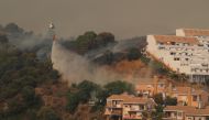 A helicopter makes a water drop over a wildfire burning near buildings on Sierra Bermeja mountain in Estepona, Spain, September 9, 2021. REUTERS/Jon Nazca
