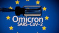 A vial and a syringe are seen in front of a displayed EU flag and words 