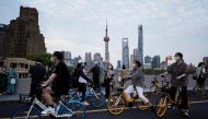 A woman wearing a protective face mask holds up her mobile phone as she stands near cyclists passing by on a bridge in Shanghai, China May 31, 2022. Reuters/Aly Song
 