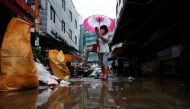  A woman using an umbrella takes photographs of a road that was flooded after torrential rain, at a traditional market in Seoul, South Korea, August 9, 2022. REUTERS/Kim Hong-Ji
