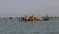 A woman and children walk as they taking refuge along a damaged road amid flood, following rains and floods during the monsoon season in Bajara village, at the banks of Manchar lake, in Sehwan, Pakistan, September 6, 2022. (REUTERS/Akhtar Soomro)