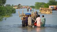 Men walk along a flooded road with their belongings, following rains and floods during the monsoon season in Sohbatpur, Pakistan, on August 28, 2022. (REUTERS/Amer Hussain)