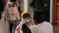 A woman arranges a face mask on a child's face in a departure terminal of the international airport in Beijing on December 29, 2022. (Photo by Noel Celis / AFP)