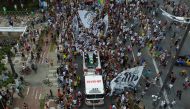 In this aerial picture fans of the late Brazilian football star Pele gather on the street as a firetruck transports Pele's coffin to the Santos' Memorial Cemetery in Santos, Sao Paulo state, Brazil on January 3, 2023.  (Photo by Miguel SCHINCARIOL / AFP)
 