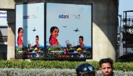 Men ride a motorbike past an Adani Group advertisement billboard in Ahmedabad on February 2, 2023. - India's beleaguered Adani group cancelled a $2.5 billion share sale on February 1, with the embattled tycoon saying it would not be 