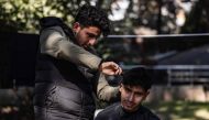 Eighteen-year-old Syrian Mohammed al-Hamo (L) cuts the hair of his 19-year-old brother Sobhi (R) in front of their tent on February 19, 2023. (Photo by Sameer Al-Doumy / AFP)