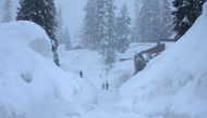 People walk down a street lined by snowbanks piled up from current and previous storms, during another winter storm in the Sierra Nevada mountains, on March 10, 2023 in Mammoth Lakes, California. Mario Tama/Getty Images/AFP 