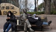 A woman leans back on a statue of South Korean novelist Yeom Sang-seop to read her newspaper, as another woman uses her phone in Seoul on March 16, 2023.
