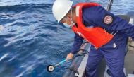 In this handout photo received from the Philippine Coast Guard and taken on March 2, 2023, a coast guard personnel collects water sample from of an oil spill in the waters off Naujan, Oriental Mindoro. Photo by Handout / Philippine Coast Guard (PCG) / AFP

