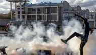 An opposition supporter kicks a teargas canister thrown by Kenya Police Officers during clashes at the informal settlement of Mathare in Nairobi, Kenya on March 27, 2023. (Photo by Luis Tato / AFP)