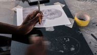 Denzel Karombe a 19-year-old school leaver who engraves portrait artworks onto polished black granite tombstones for Nyumba Yanga, a tombstone-making business uses a drill bit and tapping stone to etch a potrait at his workstation in Rugare township Harare, Zimbabwe April 21, 2023. Photo by Jekesai NJIKIZANA / AFP
