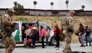 Customs and Border Protection officers walk as immigrants enter a vehicle to be transported from a makeshift camp between border walls, between the U.S. and Mexico, on May 13, 2023 in San Diego, California. (Photo by MARIO TAMA / GETTY IMAGES NORTH AMERICA / Getty Images via AFP)