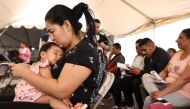 Immigrant mother Andrea, from Ecuador, holds her daughter Mia, nine months, while using her phone at a migrant transition center for asylum seekers released from Border Patrol custody after crossing into the United States, on May 12, 2023 in Somerton, Arizona. (Photo by MARIO TAMA / GETTY IMAGES NORTH AMERICA / Getty Images via AFP)
