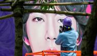 An artist refers to their phone for reference during the spray painting of a mural of K-pop megastars BTS in Seoul on June 12, 2023. (Photo by Anthony Wallace / AFP)