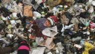 In this aerial view taken on June 3, 2023, a child smiles as she sifts through the rubbish with a scythe, looking for plastic items to sell for recycling, at a dump site near the village of Hazreh in Syria's northwestern Idlib province. (Photo by Aaref Watad / AFP)