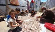 In this picture taken on June 13, 2023, Ibrahim al-Korbaw, a 48-year-old Syrian refugee and his children, shell cloves of garlic in front of the family tent at a refugee camp in Saadnayel in eastern Lebanon's Bekaa Valley. Photo by ANWAR AMRO / AFP)
