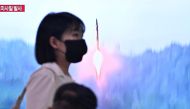 A woman walks past a television showing a news broadcast with file footage of a North Korean missile test, at a railway station in Seoul on June 15, 2023. (Photo by Anthony WALLACE / AFP)