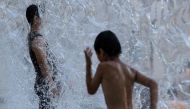 A man (L) cools off in a public water playground at a park in eastern Tokyo on July 16, 2023. (Photo by Richard A. Brooks / AFP)