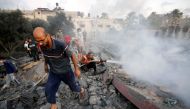 A Palestinian civil defence operator sprays water to douse the area of a building destroyed following an Israeli attack on the town of Deir Al-Balah, in the central Gaza Strip, on October 15, 2023. (Photo by Mohammed Faeq / AFP)