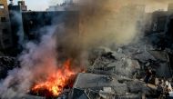 Palestinians stand on the rubble of a levelled building as smoke and fire rise from the destruction following an Israeli strike in Gaza City on October 26, 2023, amid battles between Israel and the Palestinian group Hamas. Photo by Omar El-Qattaa / AFP