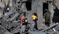 A man and woman walk carrying children past the rubble of a building hit by Israeli bombardment in Rafah in the southern Gaza Strip on October 31, 2023. (Photo by MOHAMMED ABED / AFP)