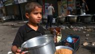 A child carries a pot as Palestinians cook in a street in Rafah in the southern Gaza Strip, on November 8, 2023. Photo by MOHAMMED ABED / AFP