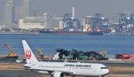 A Japan Airlines (JAL) plane taxis past as officials remove the remaining debris of a JAL passenger plane from the runway area at Tokyo International Airport at Haneda on January 5, 2024. Photo by Richard A. BROOKS / AFP