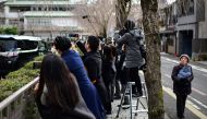A woman (R) walks past as journalists (C) try to record the departure of a vehicle as it leaves the Kyoto District Court in Kyoto on January 25, 2024, following the verdict for a Japanese man who admitted to starting a fire that killed 36 people at an animation studio in 2019. Photo by Philip FONG / AFP