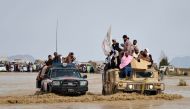Afghan men sit atop of military vehicles as they cross through a flooded area in Spin Boldak district of Kandahar province on April 13, 2024, after a flash flood following a heavy rainfall. (Photo by Sanaullah SEIAM / AFP)
