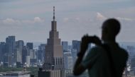 A visitor takes a photo out the window toward the 240m tall (790 ft.) NTT Docomo Yoyogi highrise building (back C) from the viewing deck at the Tokyo Metropolitan Government building in the Shinjuku area of central Tokyo on June 12, 2024. (Photo by Richard A. Brooks / AFP) 
