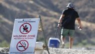 A person walks past a 'Wildfire Zone' sign on their way to cool off in the Whitewater River on July 2, 2024 in Whitewater, California. (Photo by Mario Tama/Getty Images/AFP)

