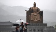 People hold umbrellas as they walk past a statue of King Sejong at the central Gwanghwamun square during rainfall in Seoul on July 18, 2024. (Photo by Jung Yeon-je / AFP)